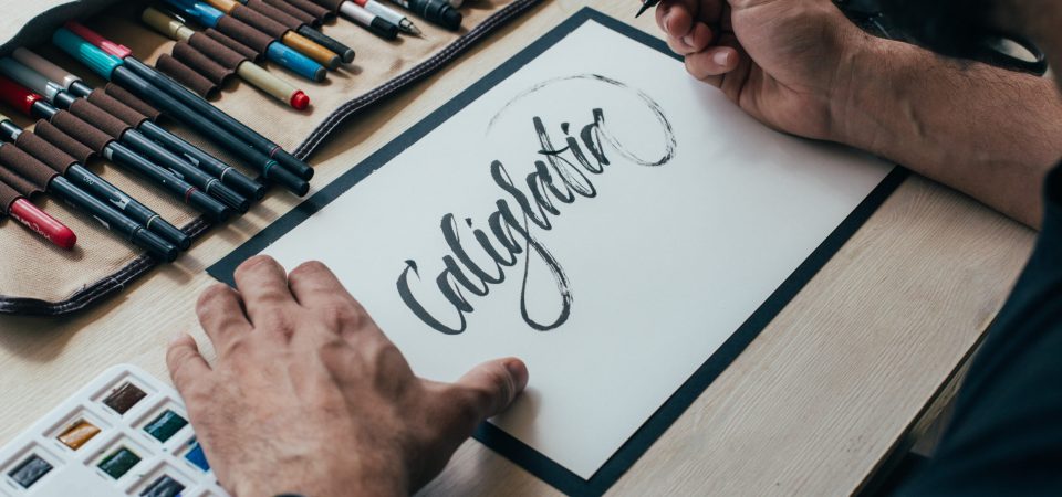 Hipster young illustrator artist in black simple tshirt creates authentic and unique hand lettering drawing in his bright industrial studio